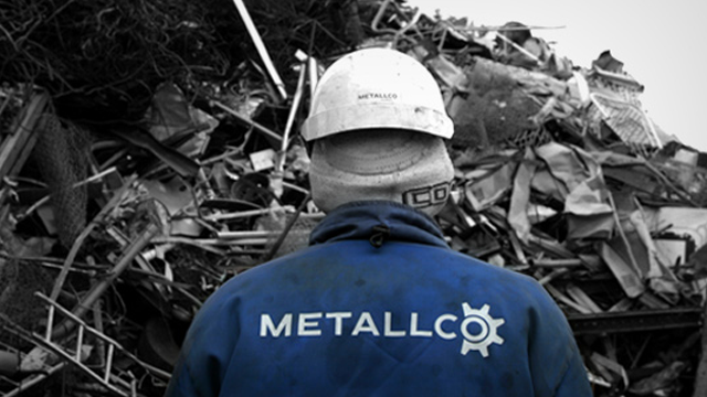 En arbeidstaker i blå jakke med logoen "METALLCO" står foran en haug med metallskrap.