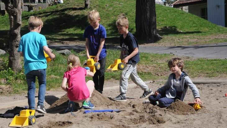 Barn leker i sandkassen, bygger med sand og leker med små lastebiler en solfylt dag i parken.