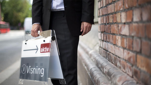 En mann i dress holder et skilt med teksten "Visning" og en pil som peker til venstre.