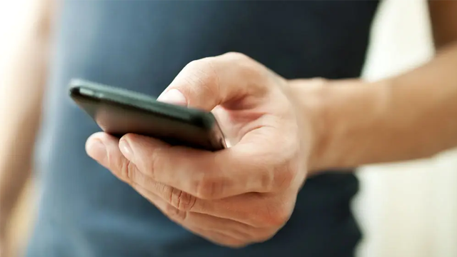 En hånd som holder en smarttelefon, med fokus på skjermen, i et lyst rom.