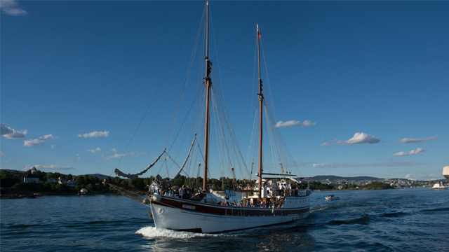 Seilbåt med to master seiler på vannet under en klar blå himmel med skyer.