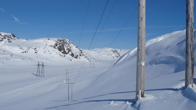 Vinterlandskap med snødekte fjell og strømledninger som strekker seg over en hvit slette.