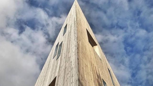 Et moderne trehus med spiss topp, mot en dramatisk skyet himmel.