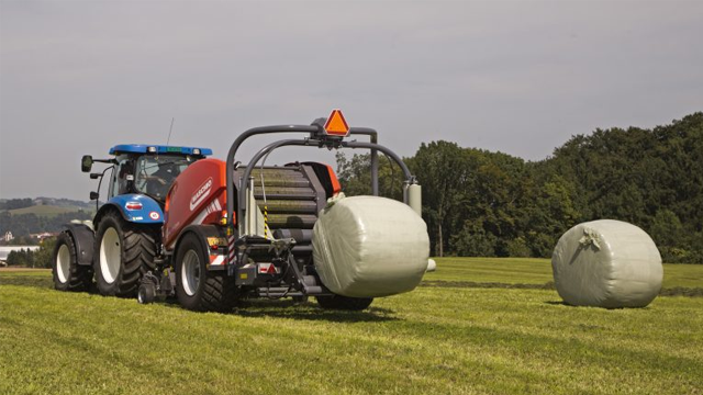 Traktor som transporterer høyballer på en grønn eng med trær i bakgrunnen.