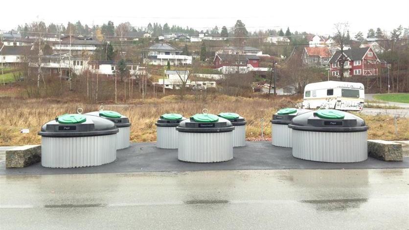 Sju avfallscontainere med grønne lokk plassert langs en vei i et boligområde.