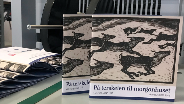 To bøker med tittelen "På terskelen til morgonhuset" ligger på et bord med trykt materiale i bakgrunnen.