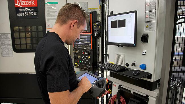 En mann som bruker en dataskjerm og kontrollpanel på en Mazak CNC-maskin.
