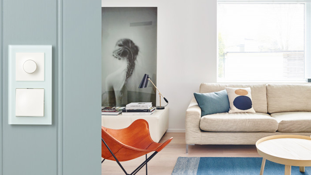 Moderne stue med lysbrytere, sofa, kunstverk på veggen og en stilren stol i skinn.