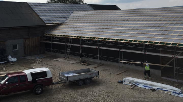 Bygning med solcellepaneler under installasjon, lastebil og tilhenger på byggeplassen.