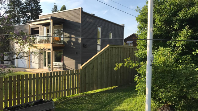 Moderne hus med balkong, gjerde og grønt gress i en solfylt hage.