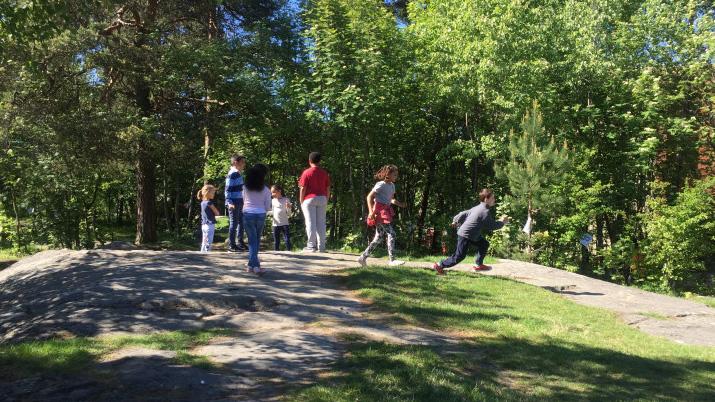 Barn som leker på en stein i en grønn park med trær i bakgrunnen. Solfylt dag.