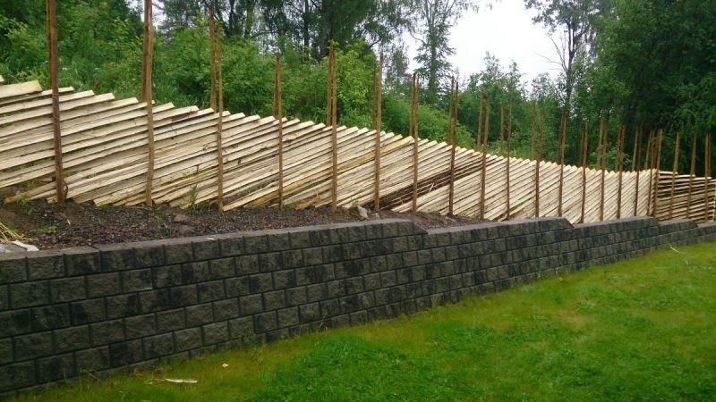 Konstruksjon av en skråning med treplanker og støttemur av stein i en hage.