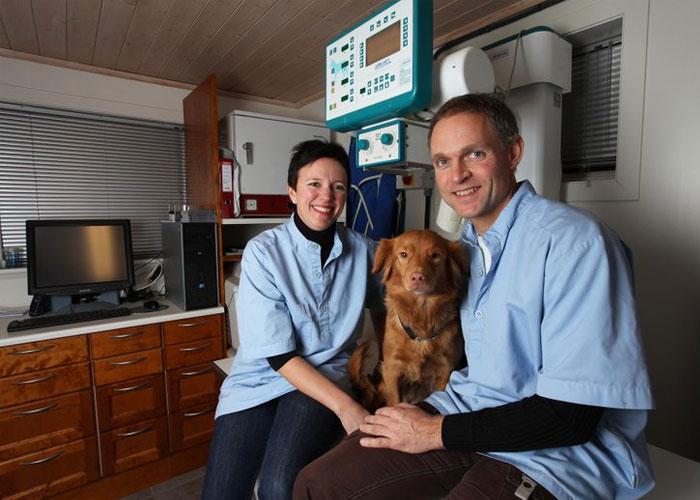 En kvinne og en mann sitter sammen med en hund i et veterinærkontor, omgitt av medisinsk utstyr.