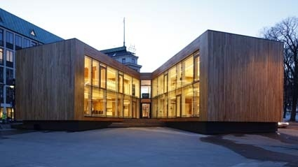 Moderne bygning med trepanel og store vinduer, beliggende i en urban setting ved skumring.