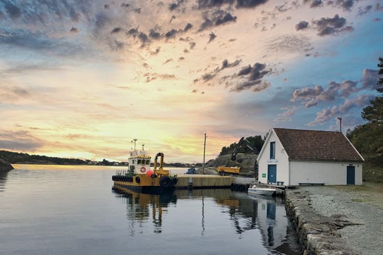 Båthavn med en gul båt ved kaien og et hvitt hus under en fargerik solnedgang.