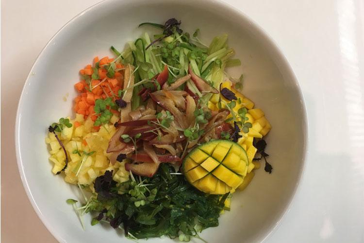 Fargerik salatbolle med mango, grønnsaker, spirer og sopp, servert i en hvit skål.