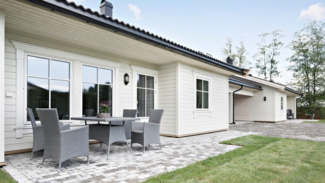 Moderne enebolig med terrasse, utemøbler og gruslagt hage i solfylt vær.