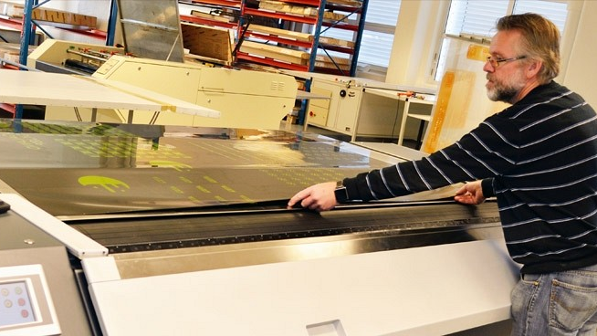 En mann som jobber med en stor skjæremaskin i et trykkeri, justerer materialet på platen.