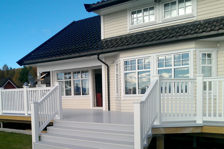 Moderne hus med hvit veranda og tak, beliggende i naturskjønne omgivelser.