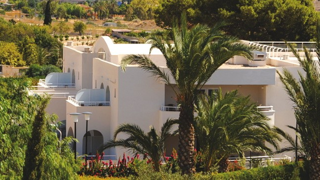 Moderne villa med palmer og grønt landskap i bakgrunnen, beliggende i et solfylt område.