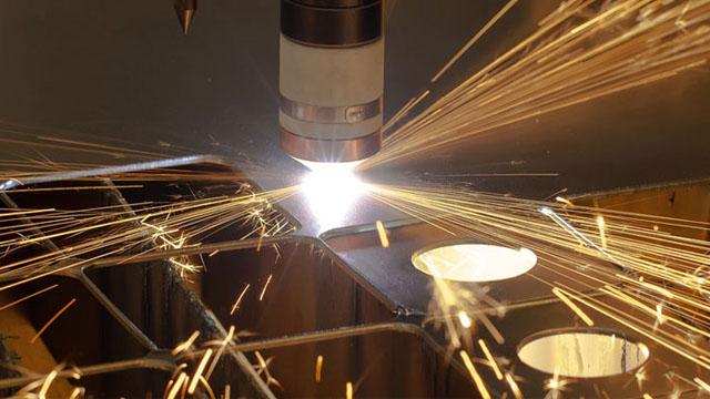 En nærbilde av en laserskjærer som kutter metallplater, med gnister som spruter ut.