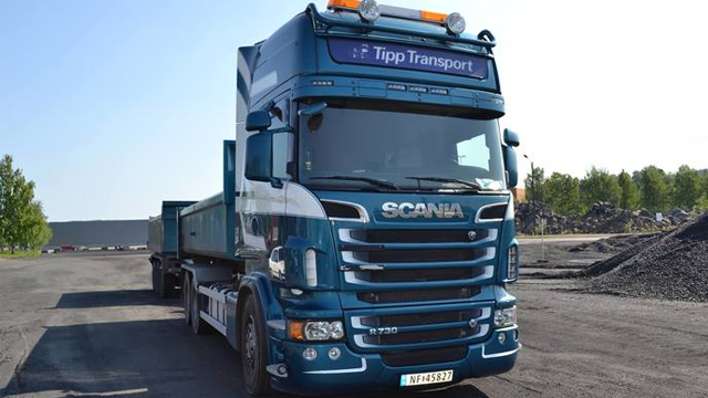 Blå Scania lastebil med Tipp Transport-logo, parkert på en grusvei med steinmateriale i bakgrunnen.