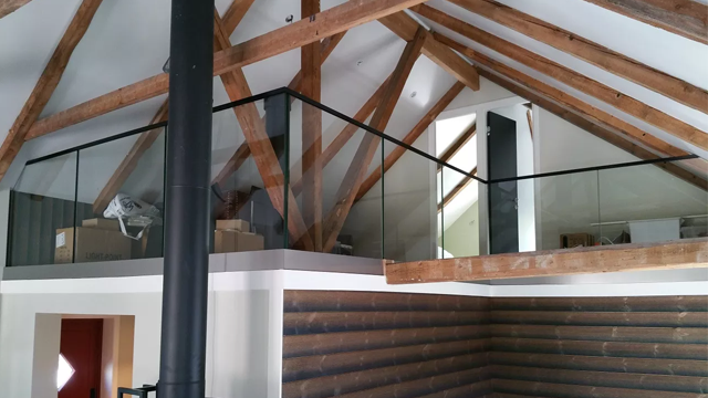 Moderne loft med synlige takbjelker, glassrekkverk og romslig plass til oppbevaring.
