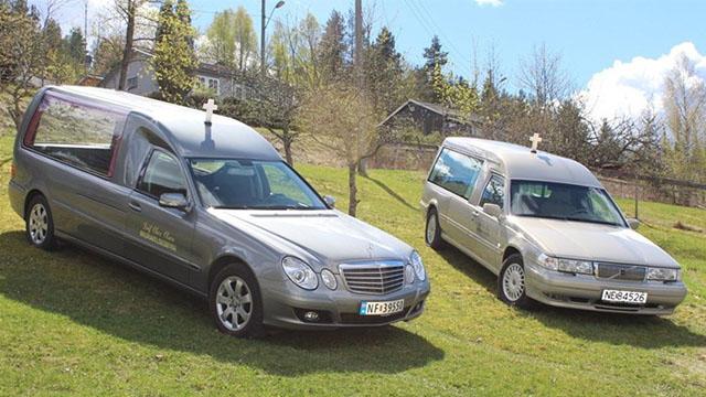 To begravelsesbiler parkert på en grønn plen med trær i bakgrunnen under en klar blå himmel.