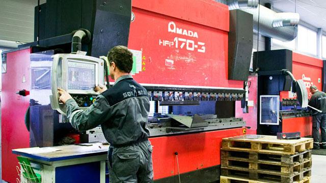 En mann som betjener en Qamada HPF-170-3 maskin i en fabrikk, med palle i forgrunnen.