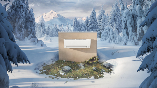 En moderne klimaanlegg installert på en vegg i en snødekt skog med fjell i bakgrunnen.