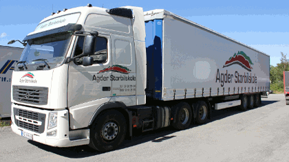 En stor lastebil med påskrift fra Agder Storbilservice står parkert på en vei.