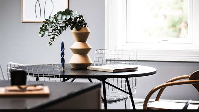 Moderne stue med et rundt bord, stoler i metall, en vase med planter og kunstverk på veggen.