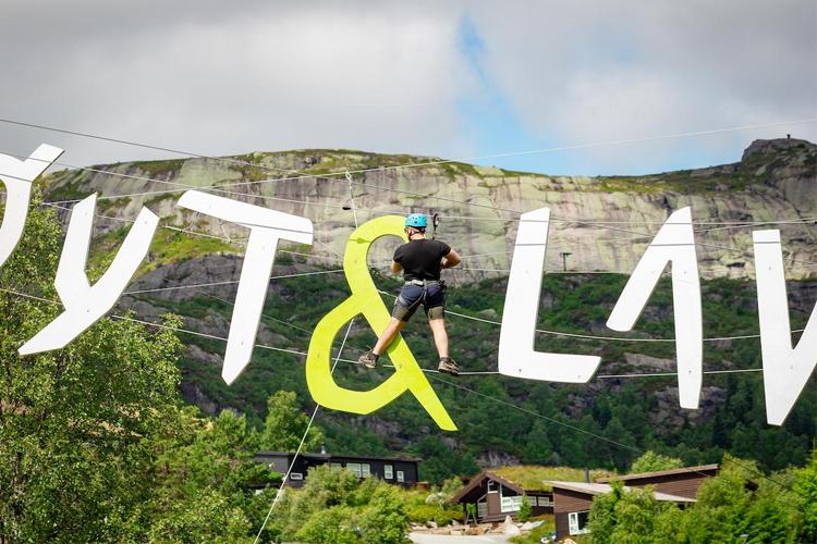 En person som balanserer på en stor, fargerik skilt med teksten "PUTT & LAV" i en naturskjønn setting.