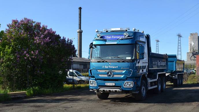Blå lastebil fra Ziegler Transport står parkert på en byggeplass med fabrikk i bakgrunnen.