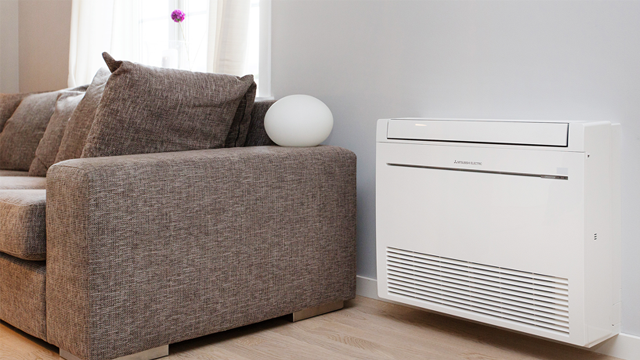 En moderne stue med en grå sofa, en hvit lampe og en veggmontert klimaanlegg.