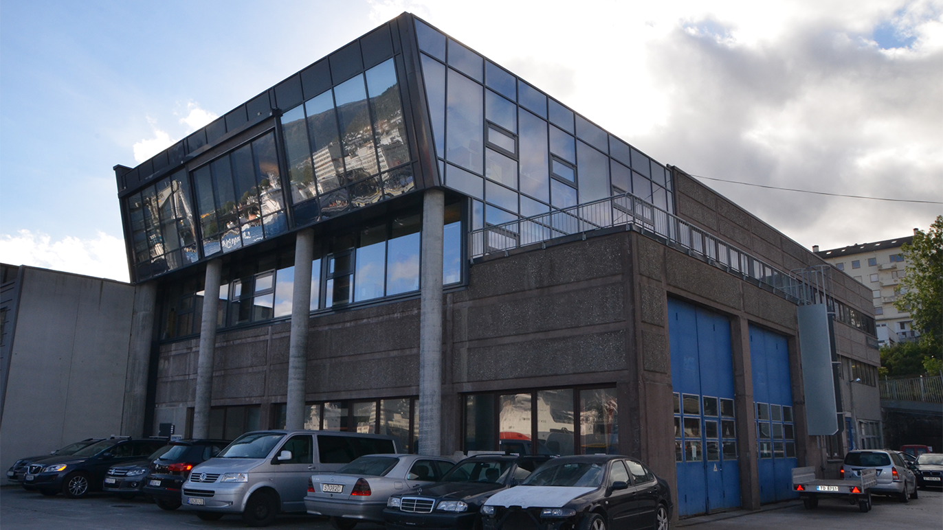 Moderne kontorbygg med glassfasade og parkerte biler foran.