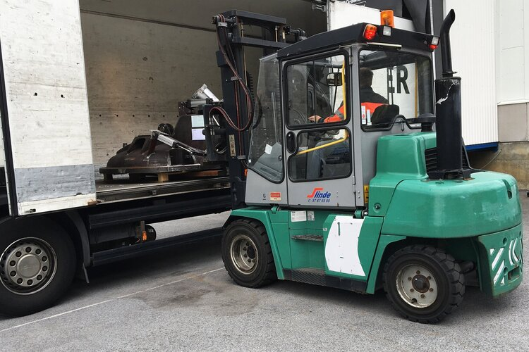 Gaffeltruck laster tungt utstyr fra en lastebil i et lagerområde.