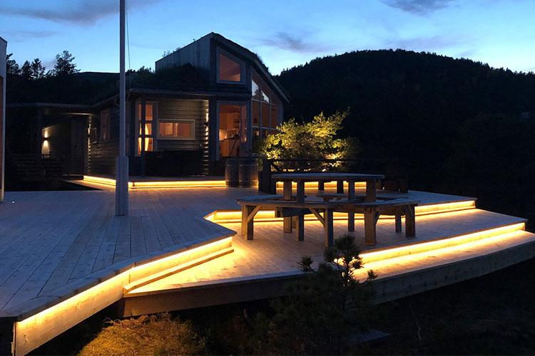 Moderne hytte med opplyst terrasse og utsikt over fjellene ved skumring.