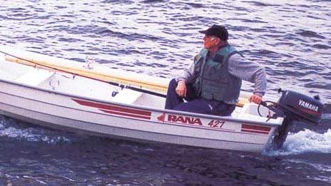 En mann i en liten båt med påhengsmotor, som kjører på vannet. Båten har en rød stripe og er merket "Rana 471".