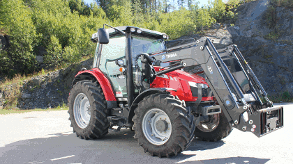 Rød traktor med frontlaster står på en grusvei omringet av trær og fjell.