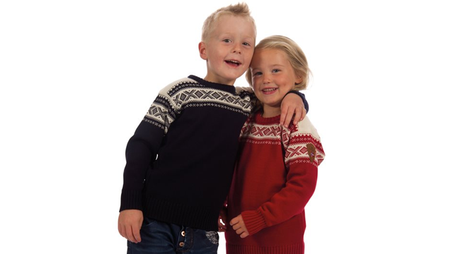 To barn i fargerike gensere med mønster, smilende og poserende sammen på en hvit bakgrunn.