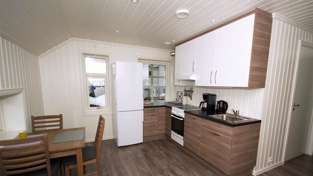 Moderne kjøkken med hvit skapinnredning, komfyr, kjøleskap og spisebord i lyst rom.