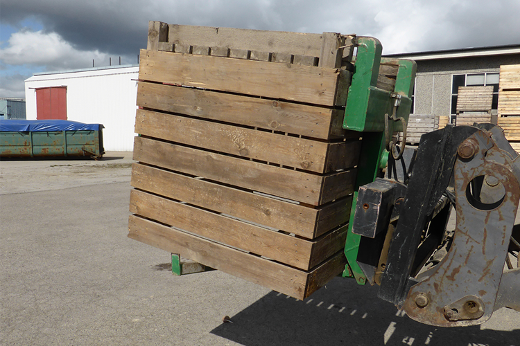 En gaffeltruck med en stor trepall på en industriell bakgrunn med bygninger og skyet himmel.