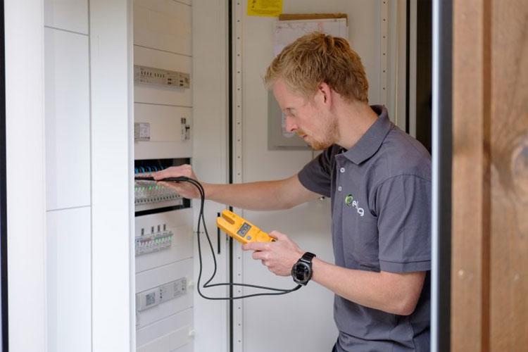 En elektriker bruker et måleinstrument for å sjekke elektriske installasjoner i et skap.