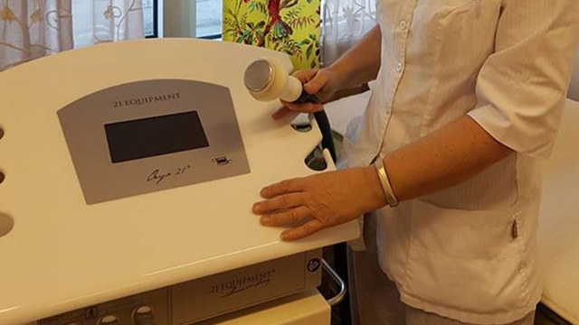 En helsearbeider bruker en ultralydmaskin i et behandlingsrom med vinduer og gardiner.
