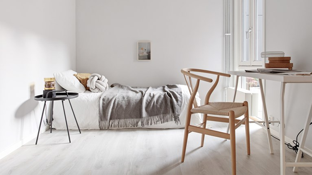 Lyst soverom med en seng, et bord, en stol og en liten sidebord med bøker og en kopp.