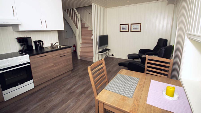 Moderne stue med kjøkken, spisebord, stoler, TV og trapp i en lys leilighet.