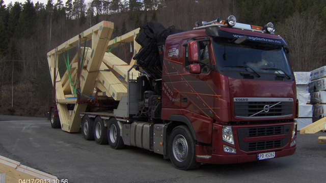 En rød Volvo lastebil med en stor trelast på tilhenger, parkert på en byggeplass i skogen.
