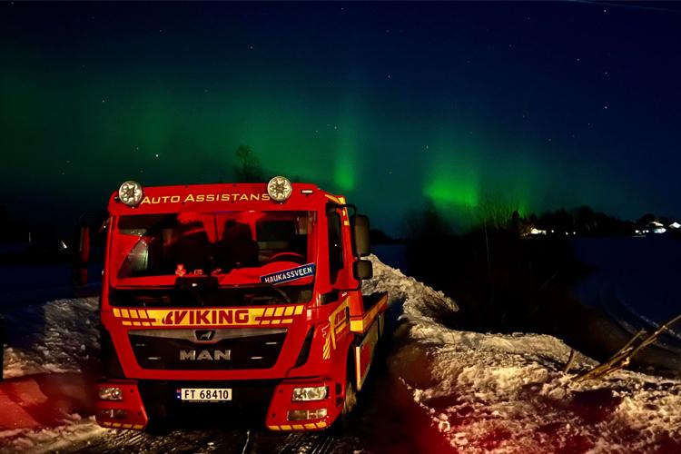 En rød bergingsbil fra Viking står på snøen under nordlyset på nattehimmelen.