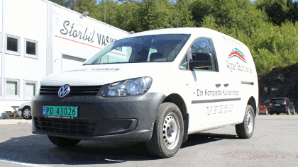 En hvit Volkswagen varebil med logoer fra Storli Vask står parkert foran en bygning.